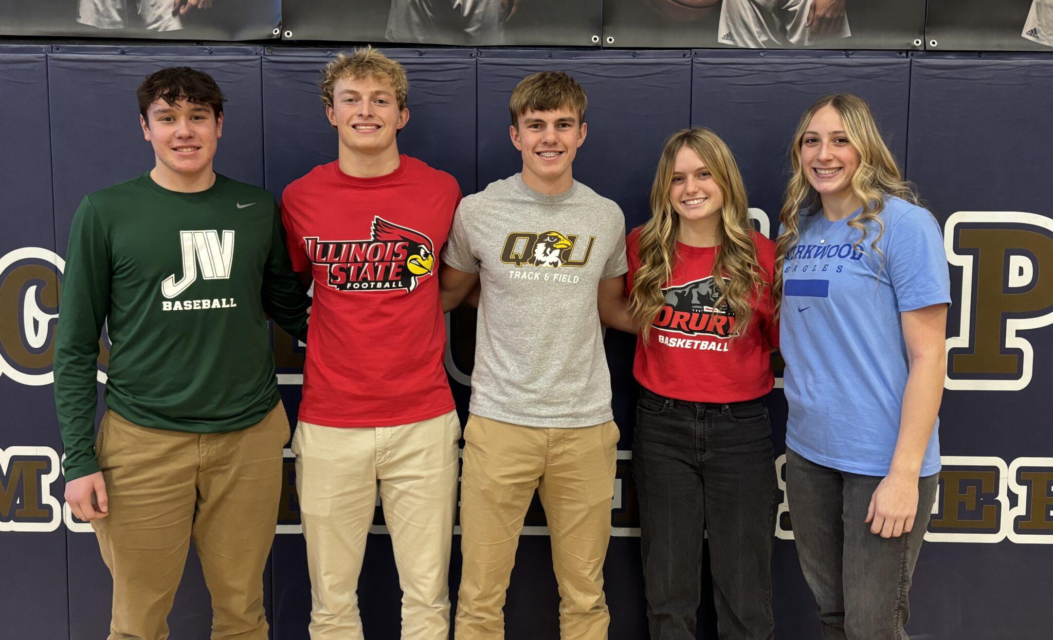 Five Quincy Notre Dame High School student-athletes posing together on signing day, wearing college shirts representing their future sports teams.