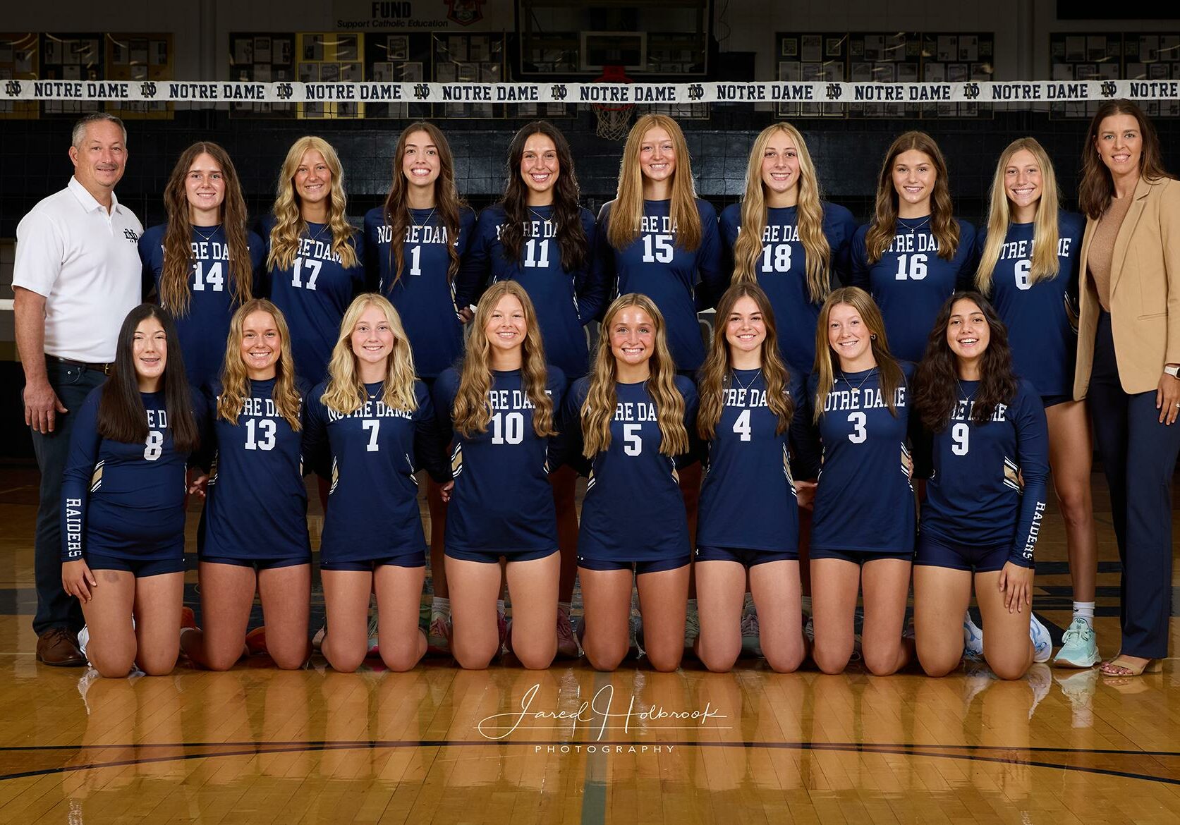 2024 Quincy Notre Dame varsity volleyball team posing in uniform on the gym floor for a team photo.