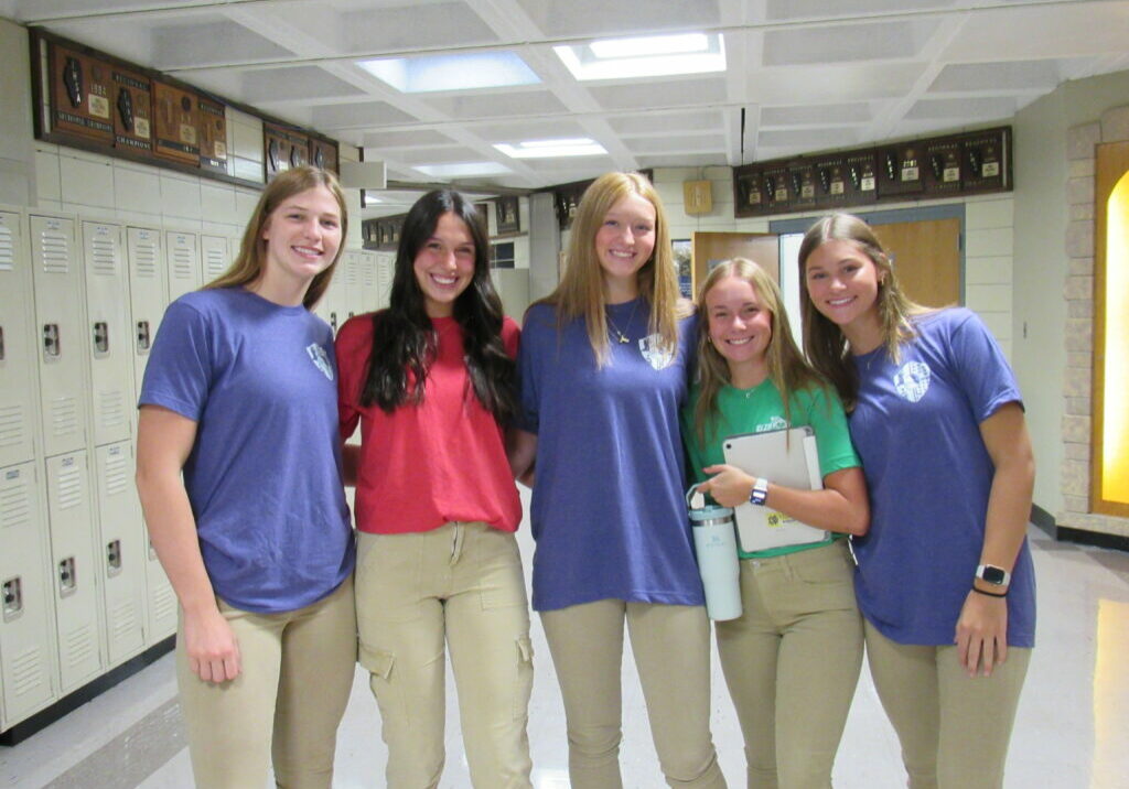 Five QND students pose in their House shirts in the hallway of QND.